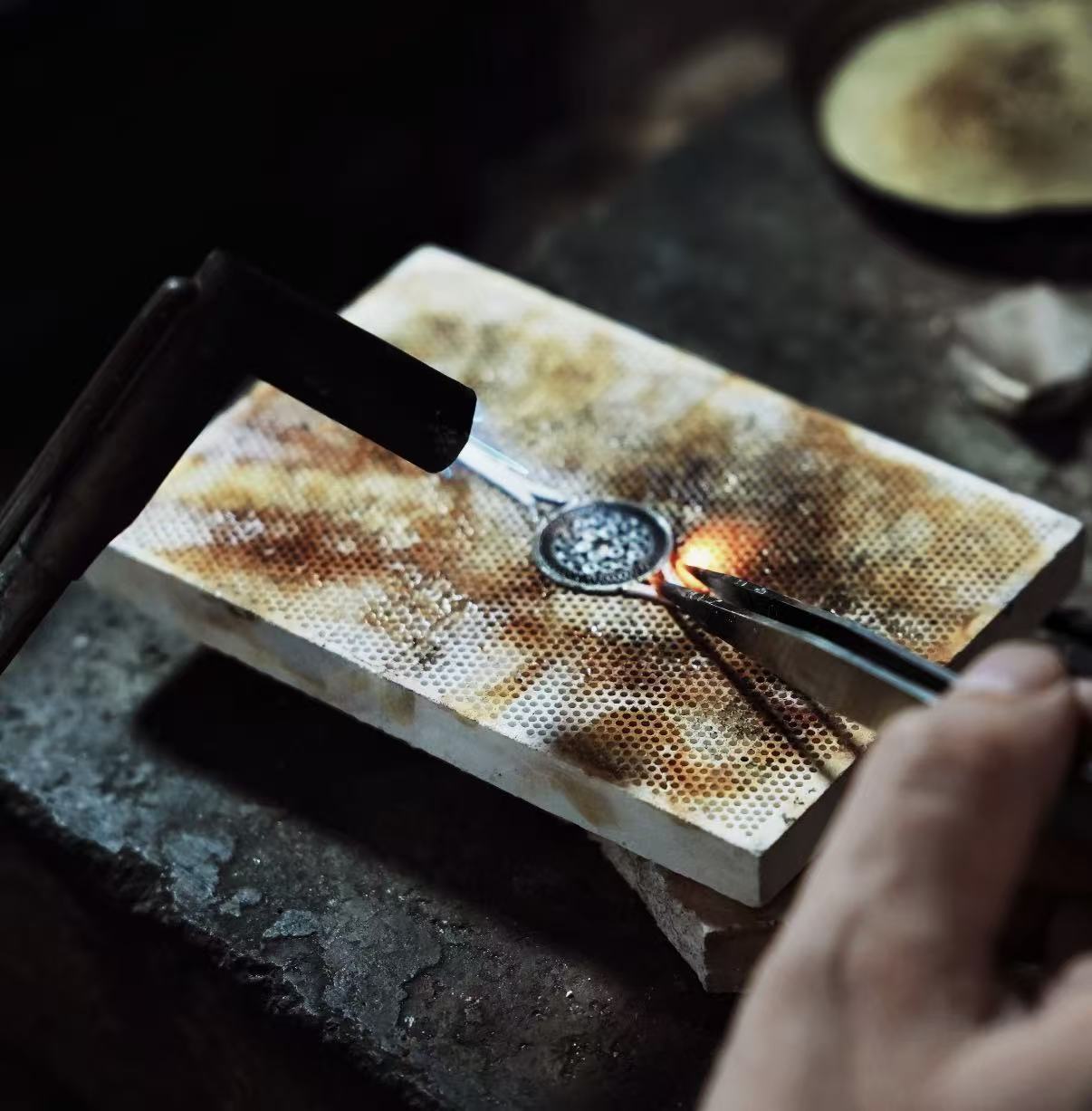 Silversmith using a torch to solder a jewelry piece in a Tibetan workshop