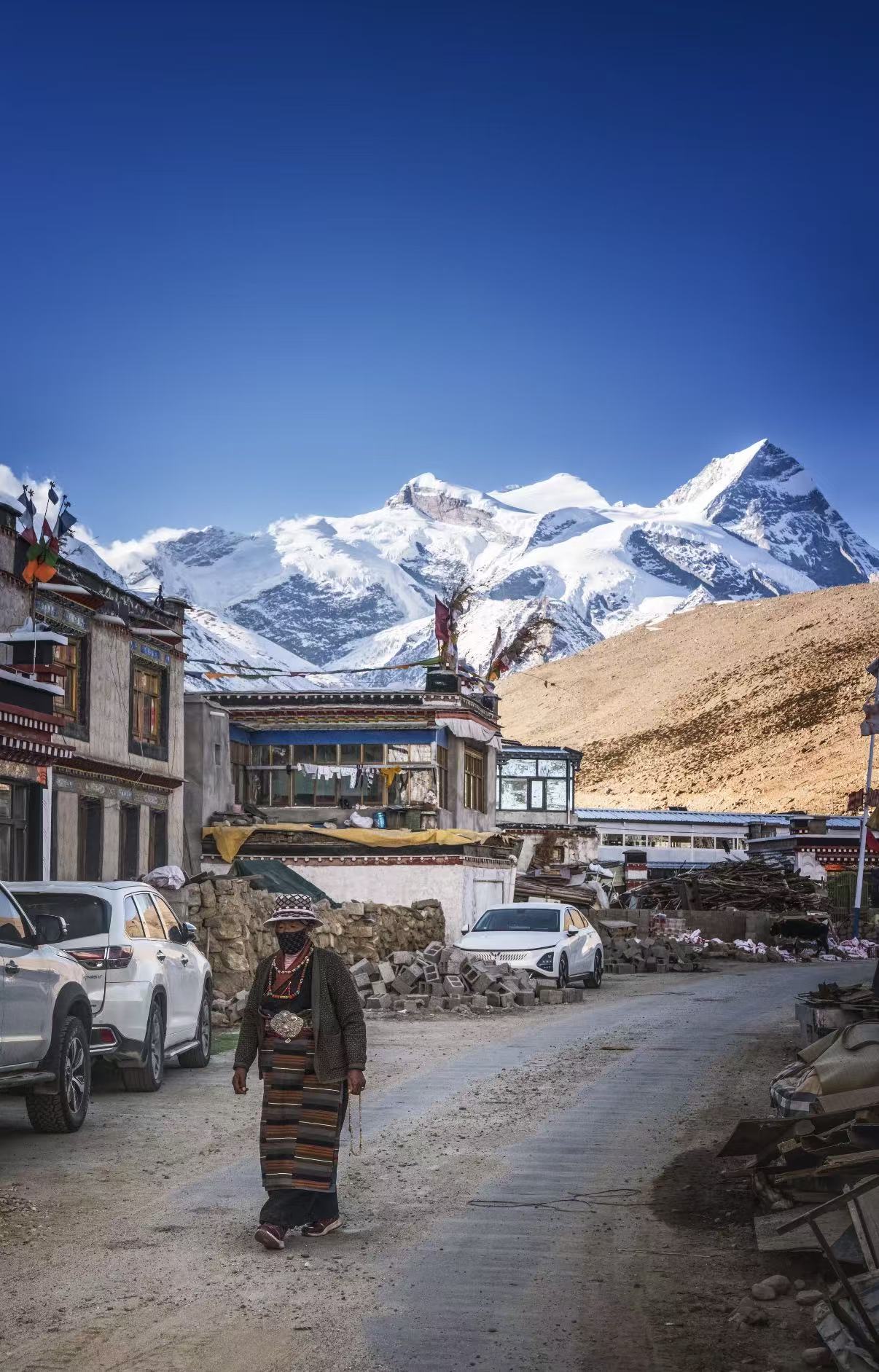 Tibetan village street with traditional-clothed resident, snow mountains ahead