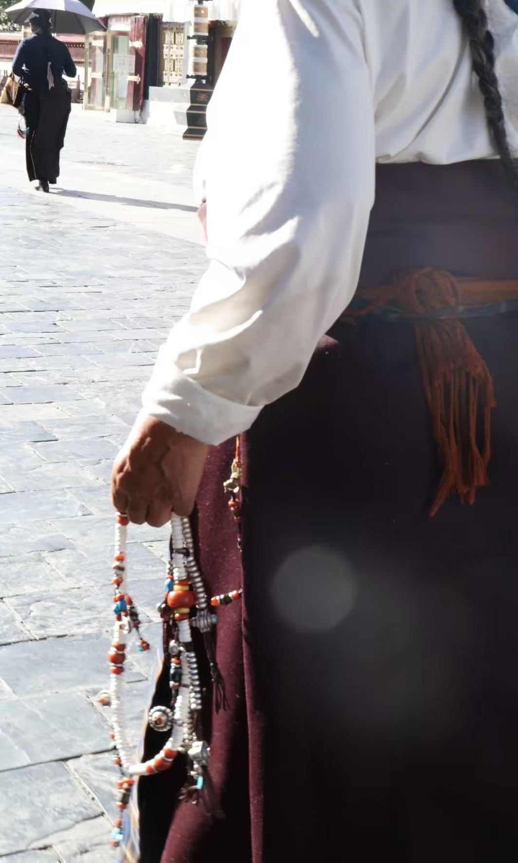 Tibetan woman at a sacred temple square, holding prayer jewelry